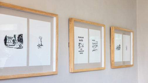 Three black and white prints framed in light wood are displayed in a line on a cream wall.